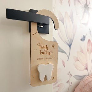 May include: Wooden door hanger with the text "Tooth Fairy, please stop here" and a white tooth cutout. The hanger is decorated with gold stars.