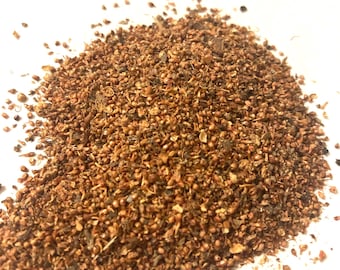 May include: A close-up of a pile of brown and red dried herbs and seeds. The herbs and seeds are scattered on a white surface.