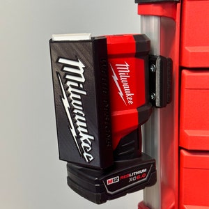 May include: A red Milwaukee M12 RedLithium XC6.0 battery is attached to a black and gray battery holder. The battery holder is attached to a red and black tool box.