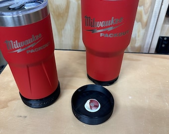 May include: Two red insulated tumblers with black lids and a black lid on a wooden surface. The tumblers have the Milwaukee Packout logo on them.