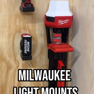 May include: Two Milwaukee light mounts, one red and black with a white light, and one red and black with a white light and a black handle. The mounts are attached to a wooden wall. The text "MILWAUKEE LIGHT MOUNTS" is written in white letters on a black background.