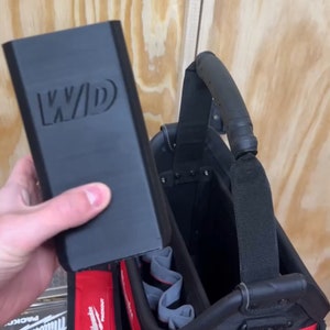May include: A black tool bag with a red and black strap. The bag has a handle and a zipped compartment. The bag is labelled "Milwaukee" and has a "3x3 XL BIN!" label on the side.