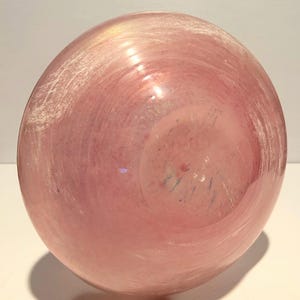 Puede incluir: Un jarr&oacute;n de vidrio rosa con un acabado texturizado e iridiscente. El jarr&oacute;n tiene una forma redonda y una abertura ancha.