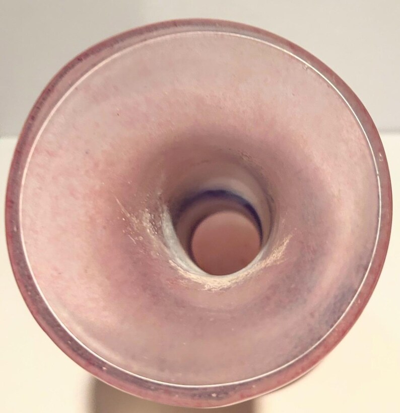 Puede incluir: El interior de un jarr&oacute;n de vidrio rosa con una abertura ancha. El jarr&oacute;n tiene un acabado liso y brillante.