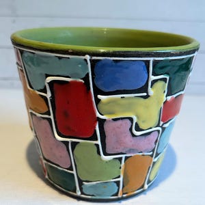 May include: A green ceramic planter with a black and white geometric design. The planter is decorated with colorful squares and rectangles in shades of red, blue, yellow, green, pink, and orange.