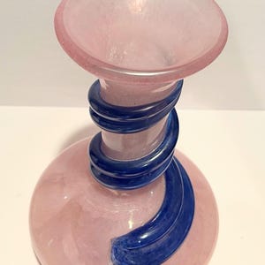 Puede incluir: Un jarr&oacute;n de vidrio rosa con un dise&ntilde;o de espiral azul. El jarr&oacute;n tiene una base ancha y un cuello estrecho.