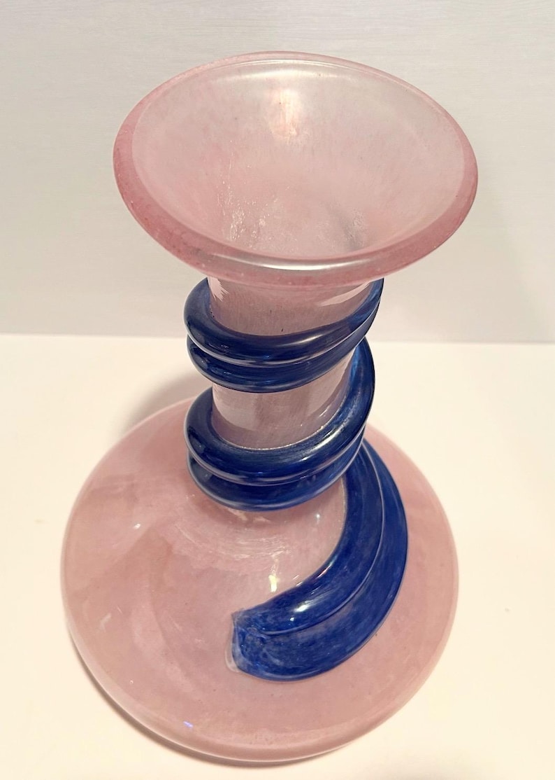Puede incluir: Un jarr&oacute;n de vidrio rosa con un dise&ntilde;o de espiral azul. El jarr&oacute;n tiene una base ancha y un cuello estrecho.
