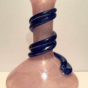 Puede incluir: Un jarr&oacute;n de vidrio rosa con un dise&ntilde;o de vidrio azul oscuro en espiral alrededor del cuello.