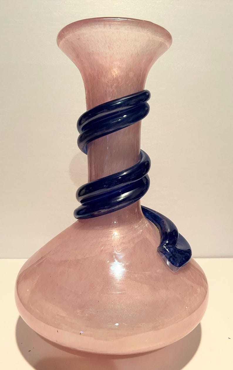 Puede incluir: Un jarr&oacute;n de vidrio rosa con un dise&ntilde;o de vidrio azul oscuro en espiral alrededor del cuello.