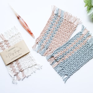 May include: Handmade crochet coasters in white, pink, and blue with fringe detail. One set is wrapped with a brown paper label that reads "Handmade My Rugs 100% Cotton Yarn". A crochet hook with a marbled handle is also present.