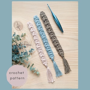May include: Three crochet bookmarks in pink, blue, and brown with matching tassels, and a blue crochet hook. The bookmarks are displayed on a wooden surface with the text "crochet pattern" in a pink circle.