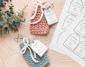 Può includere: Due sacchetti per sapone all'uncinetto fatti a mano, uno rosa e uno blu, con cordini bianchi ed etichette. Le etichette recitano "Handmade Soap Saver" e "Handmade with love". È visibile anche un foglio di etichette stampate.