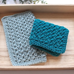 May include: Two crocheted dishcloths in a wooden tray. One dishcloth is teal blue and the other is light grey.