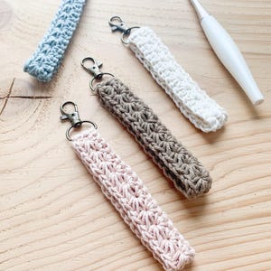 May include: Four crocheted keychains in different colors: light blue, white, brown, and pink. Each keychain has a metal clasp and is made with a delicate stitch pattern.