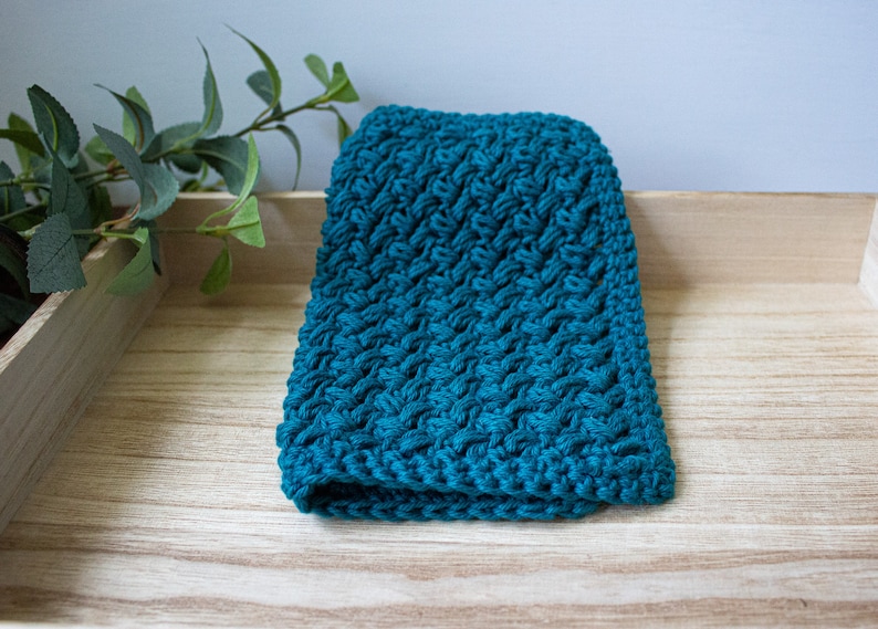 May include: A teal blue knitted dishcloth with a textured pattern. The dishcloth is sitting on a wooden surface.