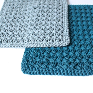 May include: Two crocheted squares, one in a light grey colour and one in a teal blue colour. The squares are made with a textured stitch pattern.
