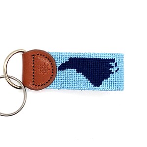 Peut inclure: Un porte-cl&eacute;s bleu et bleu marine avec une boucle en cuir orn&eacute;e d'une boussole. Le porte-cl&eacute;s est tiss&eacute; avec le contour de l'&eacute;tat de Caroline du Nord.
