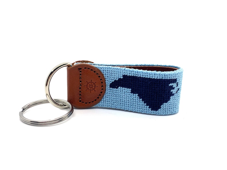 Peut inclure: Un porte-cl&eacute;s bleu clair et bleu marine avec une sangle en cuir et un anneau en m&eacute;tal. La sangle pr&eacute;sente un motif tiss&eacute; de l'&eacute;tat de Caroline du Nord. La sangle en cuir a un petit motif de boussole en relief.