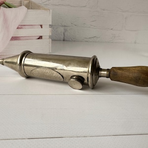 Vintage air pump by the French brand Perolin shown in side view, an antique grease pump with metal body and wooden handle, industrial decor and collectible antique tool