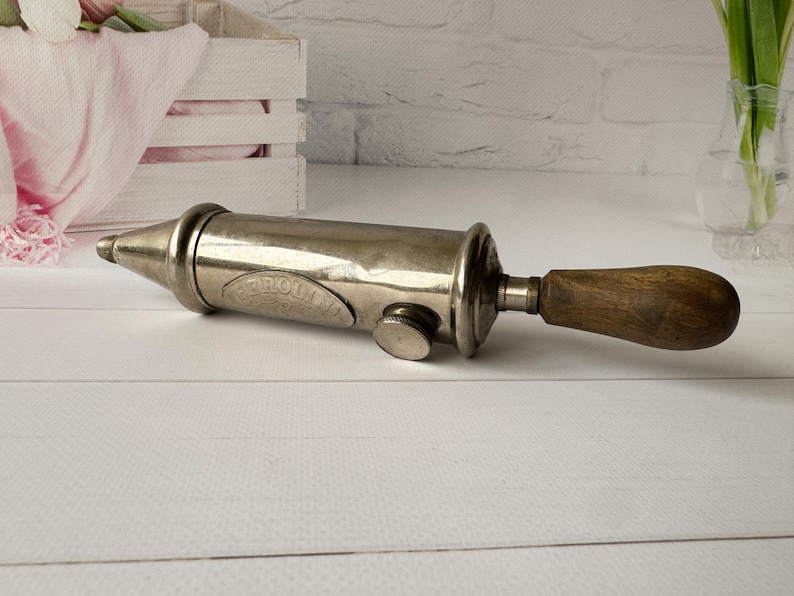 Vintage air pump by the French brand Perolin shown in side view, an antique grease pump with metal body and wooden handle, industrial decor and collectible antique tool