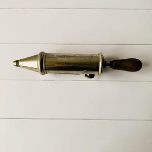 Antique grease pump Perolin photographed from above, vintage lubrication tool with metal body and wooden handle, showing authentic signs of age