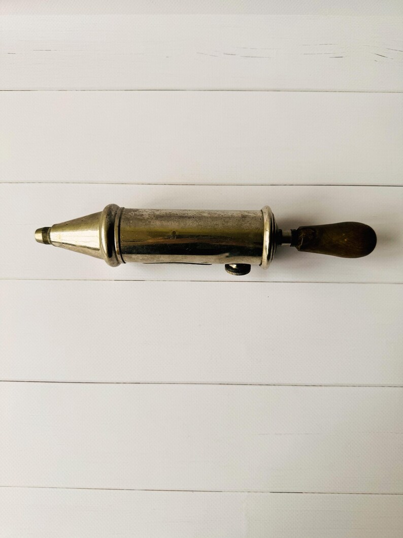 Antique grease pump Perolin photographed from above, vintage lubrication tool with metal body and wooden handle, showing authentic signs of age