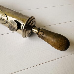 Detail of the rear section and wooden handle of a vintage grease gun Perolin, showing aged wood and metal construction