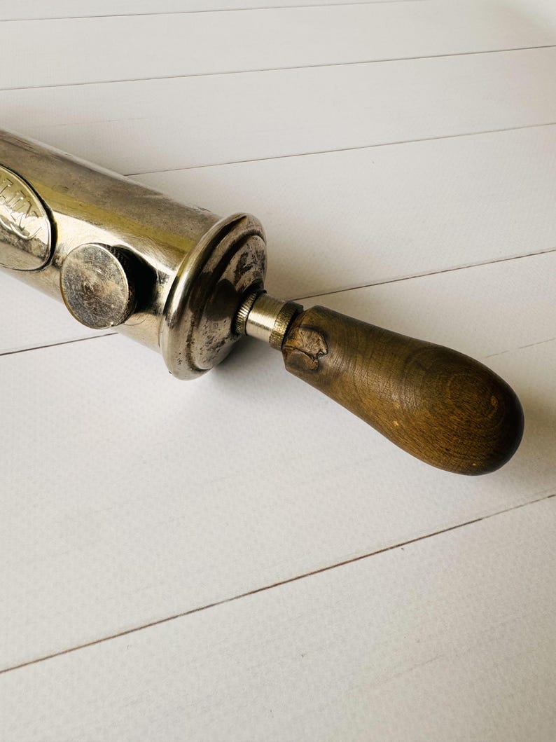 Detail of the rear section and wooden handle of a vintage grease gun Perolin, showing aged wood and metal construction