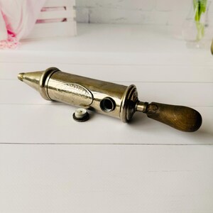 Vintage grease gun Perolin with visible opening and cap, antique grease pump detail photo showing mechanical construction and metal finish
