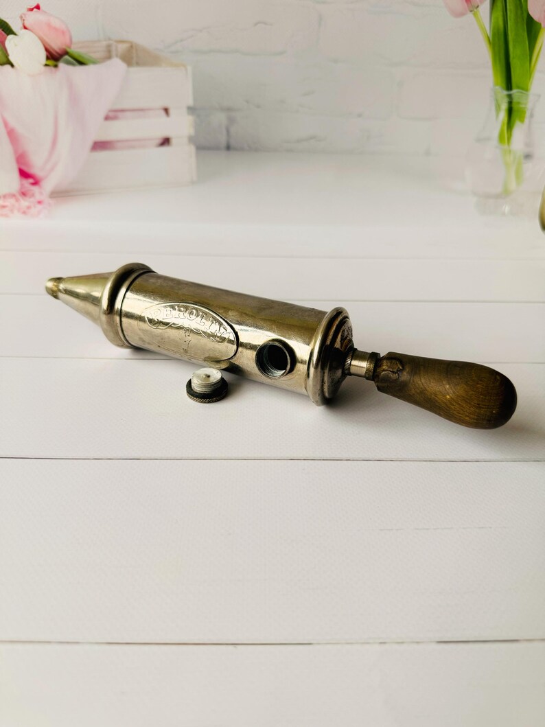 Vintage grease gun Perolin with visible opening and cap, antique grease pump detail photo showing mechanical construction and metal finish