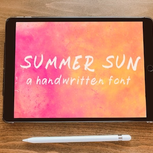 Puede incluir: Una tableta negra muestra las palabras "SUMMER SUN" y "a handwritten font" en blanco sobre un fondo de acuarela rosa y naranja. Un lápiz óptico blanco descansa debajo sobre una superficie de madera.
