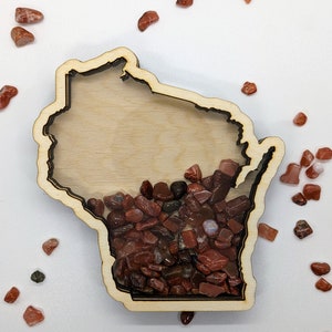 May include: A wooden cutout of the state of Wisconsin filled with small red and brown stones.