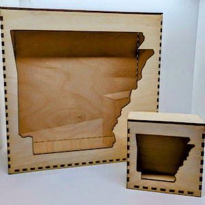 Puede incluir: Dos cajas de sombra de madera con un recorte del estado de Arkansas. La caja más grande está a la izquierda y la más pequeña a la derecha.