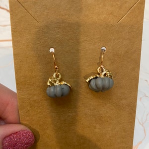 May include: A pair of gray pumpkin-shaped dangle earrings with gold accents. The earrings are displayed on a brown card.