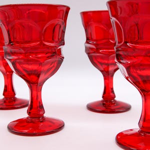 May include: Four red glass goblets with a textured design. The goblets are arranged in a row, with the one in the foreground slightly out of focus.