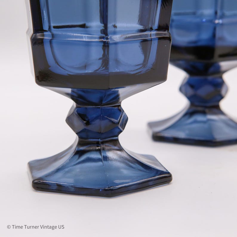 May include: Two deep blue glass goblets featuring a faceted, geometric design with a hexagonal base and a multi-faceted stem. The glassware has a distinct angular profile and a rich, translucent cobalt color throughout the entire structure.