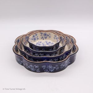 May include: A set of four nested ceramic serving dishes. Each dish is navy blue with a scalloped edge and a floral design in white. The rims are trimmed with a brown beaded border. The dishes are arranged in a nested configuration.