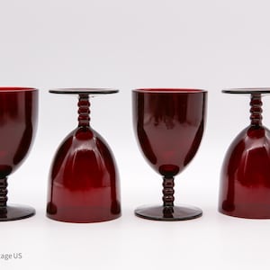 May include: Four vintage ruby red wine glasses. The glasses have a rounded bowl shape, a twisted stem, and a flat base. Two glasses are upright, and two are inverted. The glasses are made of glass.