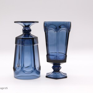 May include: Two deep blue glass goblets with a faceted, paneled design. One goblet stands upright on a hexagonal base with a short, thick stem, while the other is inverted, resting on its flat rim to display the base and stem structure clearly.