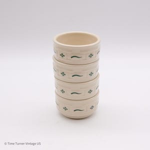May include: A stack of four off-white ceramic bowls. Each bowl features a repeating pattern of green floral and curved line designs. The bowls are stacked on top of each other, showcasing their round shape and decorative details.