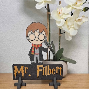 May include: A black desk sign with a gold inscription that reads "Mr. Filbert". A cartoon character of Harry Potter with a wand stands above the sign.