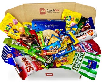 Può includere: Una scatola di cartone etichettata CzechBox riempita con vari snack cechi e slovacchi, tra cui Kofola, cialde Opavia, Fidorka, Margot e caramelle Slavia. L'assortimento presenta involucri di plastica colorati con testo in ceco e slovacco.