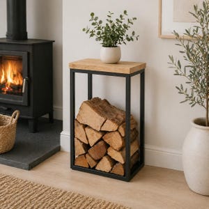 May include: A rectangular firewood storage unit with a black metal frame and a light wood top. The unit is filled with logs. A small plant in a pot sits on top. The unit is near a fireplace.