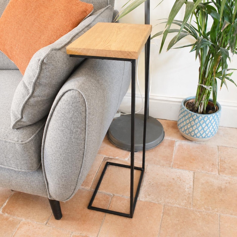 Pu&ograve; includere: Un tavolino con piano rettangolare in rovere e struttura in metallo nero. Il tavolo &egrave; progettato per essere posizionato accanto a un divano. Le dimensioni del tavolo sono di circa 30 cm di larghezza, 46 cm di lunghezza e 61 cm di altezza.