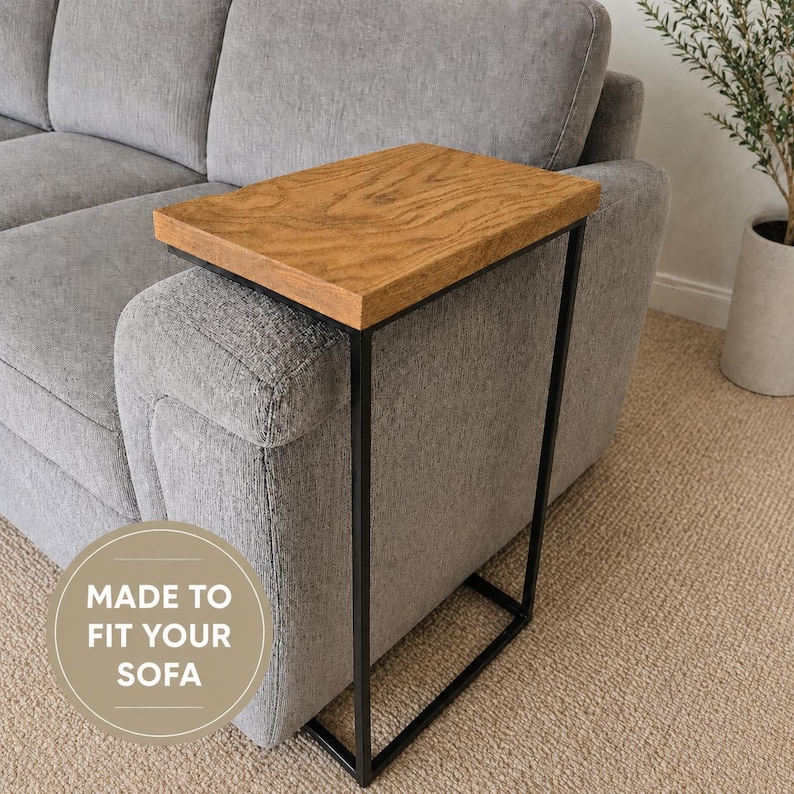 Pu&ograve; includere: Un tavolino in legno con piano rettangolare e struttura in metallo nero. Il piano ha una finitura a venatura naturale. Il testo "MADE TO FIT YOUR SOFA" &egrave; in un cerchio. Progettato per divani.