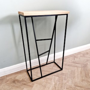 May include: A contemporary side table featuring a rectangular light wood top and a black metal frame. The frame has a geometric design with angled legs and supporting bars. The table is approximately 76 cm tall.