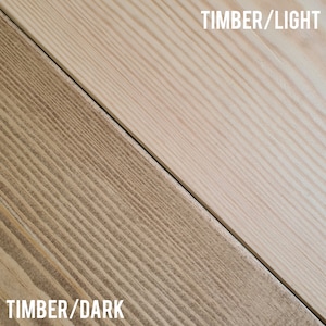 Pu&ograve; includere: Vista diagonale di due assi di legno, una chiara e una scura. L'asse chiaro &egrave; di colore legno naturale chiaro, mentre l'asse scuro &egrave; di un marrone caldo. Testo: "TIMBER/LIGHT" e "TIMBER/DARK".