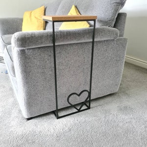 May include: A black metal side table with a wooden top and a heart-shaped cutout in the frame. The table is next to a grey sofa.