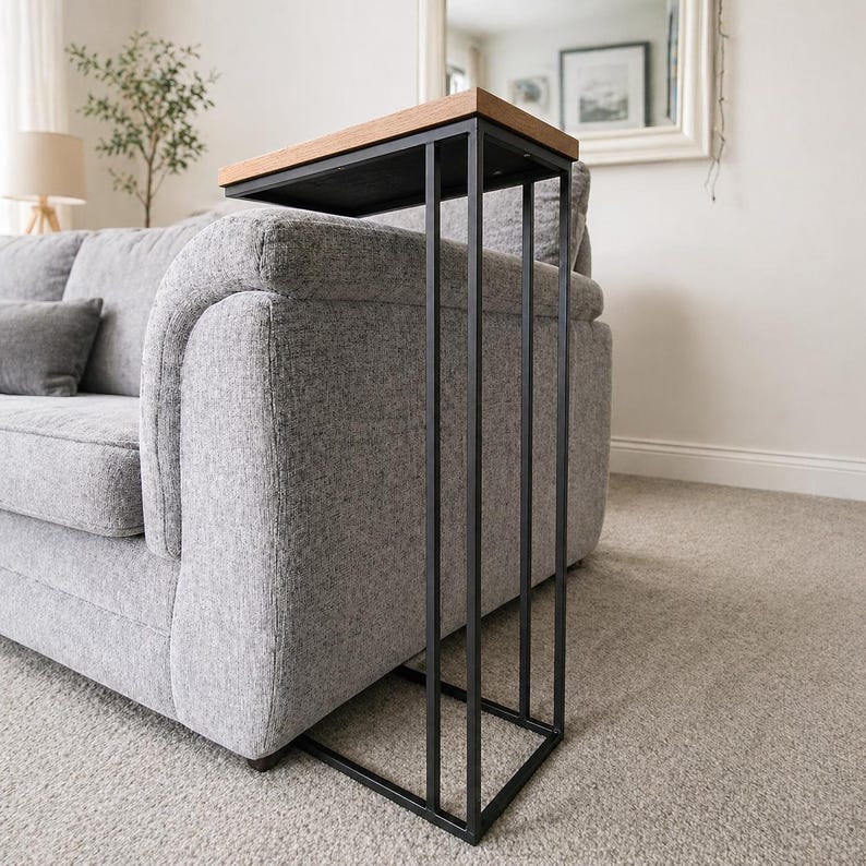 May include: A modern side table with a black metal frame and a rectangular wooden top. The table is designed to slide alongside a sofa, offering a convenient surface for drinks or decor. The table's dimensions are approximately 20 inches long, 10 inches wide, and 24 inches high.