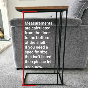 May include: A side table with a rectangular, light brown wooden top and a black metal frame. The table is designed to slide under a sofa. The text on the image says, "Measurements are calculated from the floor to the bottom of the shelf."